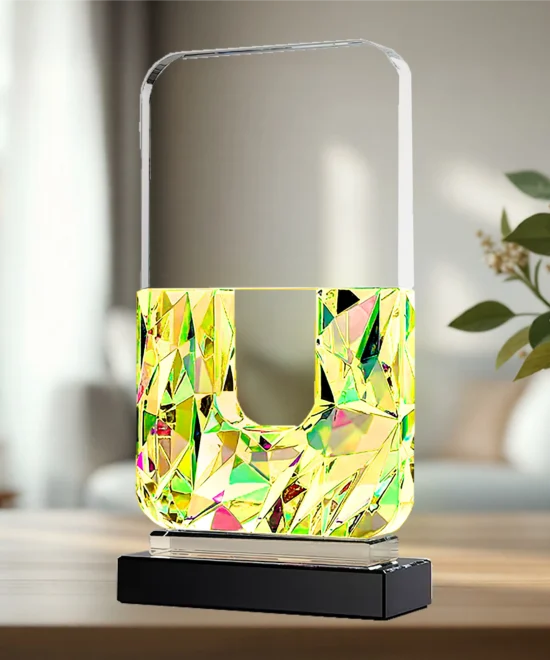 Abstract geometric glass sculpture with a pale frame top and a multicolored mosaic body on a black pedestal.