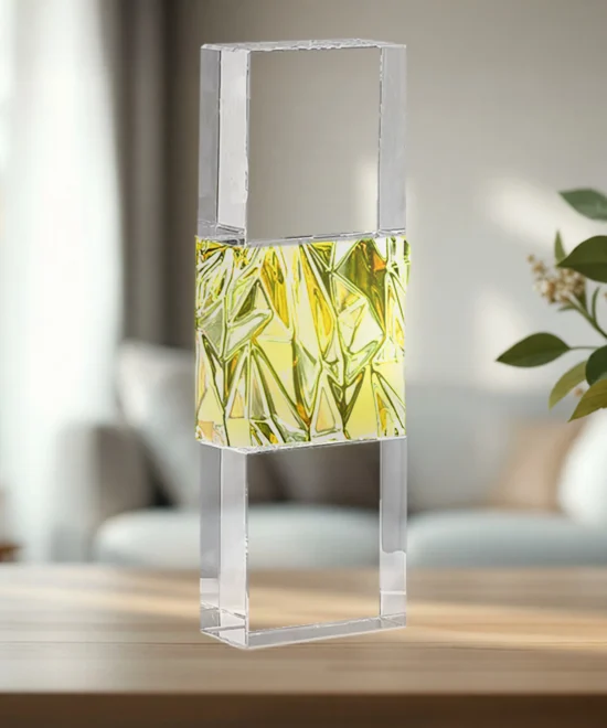 Clear rectangular glass block mounted on a metal frame, with a yellow-green faceted interior, on a wooden table
