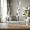 Clear, angular glass-like chairs arranged along a wooden surface in a bright room.